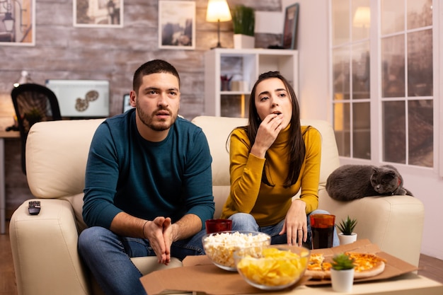 Couple cheering for their favourite team while watching TV and eating fast food