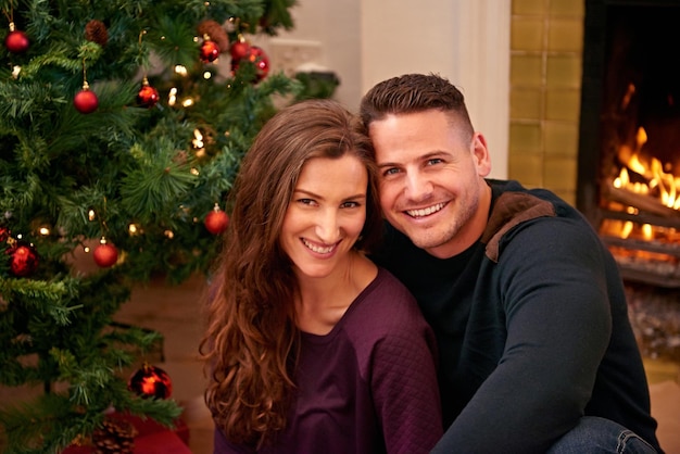 Couple christmas and portrait together in home with smile happiness and bonding with christmas tree Man woman and happy by fireplace for celebration party and holiday spirit on living room floor