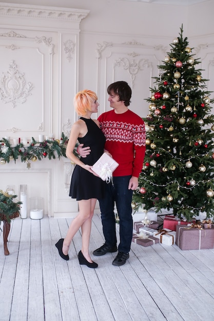 Couple on Christmas time with gifts box in their living room, in front of the Christmas tree