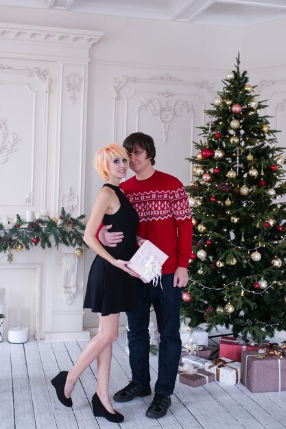 Couple on Christmas time with gifts box in their living room, in front of the Christmas tree