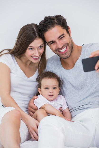 Couple clicking selfie with baby on bed 