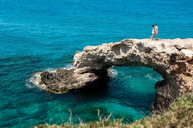 The couple on the cliff by the sea. Honeymoon lovers. Man and woman traveling. Couple in love on vacation. Newly married couple. Wedding travel. Honeymoon trip. Man and woman kissing by the sea