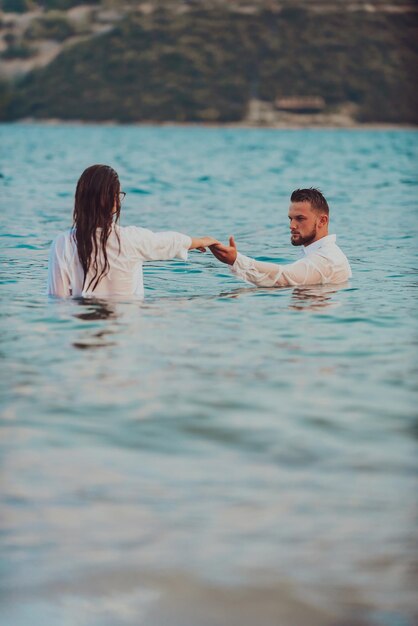 A couple in clothes holding hands in the sea. High quality photo