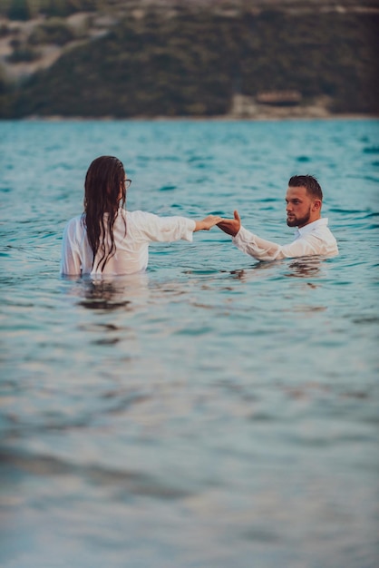 A couple in clothes holding hands in the sea. High quality photo