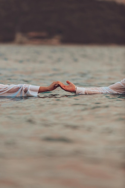 A couple in clothes holding hands in the sea. High quality photo