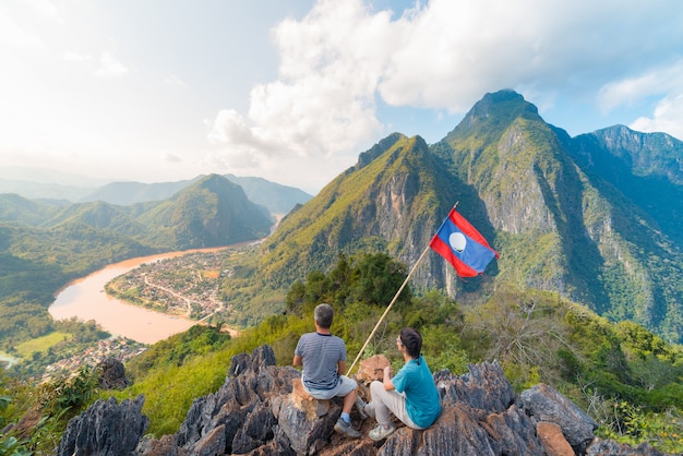 Couple conquering mountain top at Nong Khiaw panoramic view over Nam Ou River valley Laos national flag scenic mountain landscape