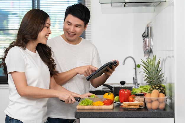 Couple cooking and preparing vegetables according to a recipe on a tablet computer in kitchen at home