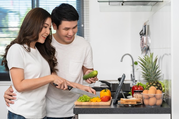 Couple cooking and preparing vegetables according to a recipe on a tablet computer in kitchen at home