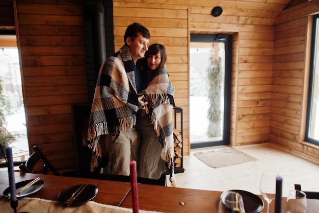 Couple covered blanket in modern wooden house spending time together in warm and love