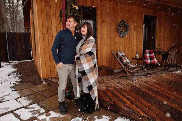 Couple covered blanket in winter day spending time together in love against wooden house