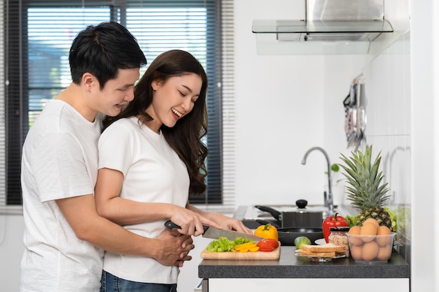 Couple cutting vegetables for preparing healthy food in the kitchen at home man is hugging woman