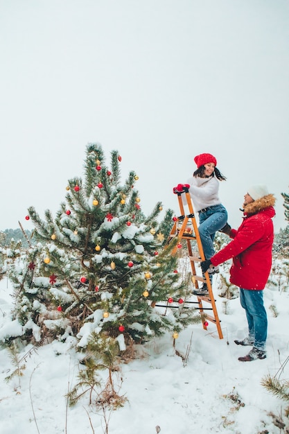 Couple decorating christmas tree outdoors snowed winter outdoors