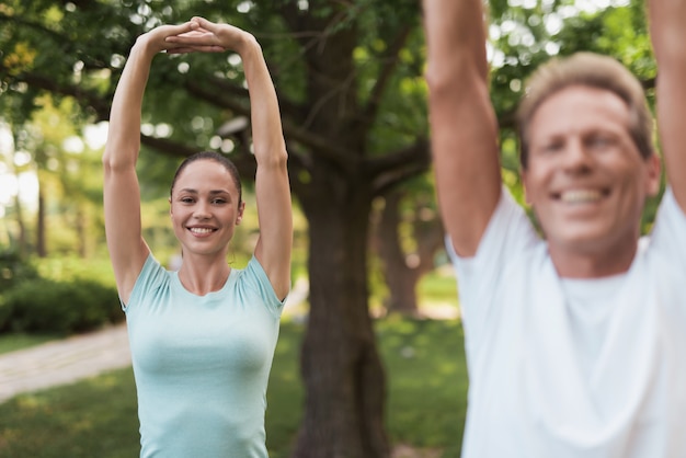 Couple doing exercises in park. They do stretching hands.