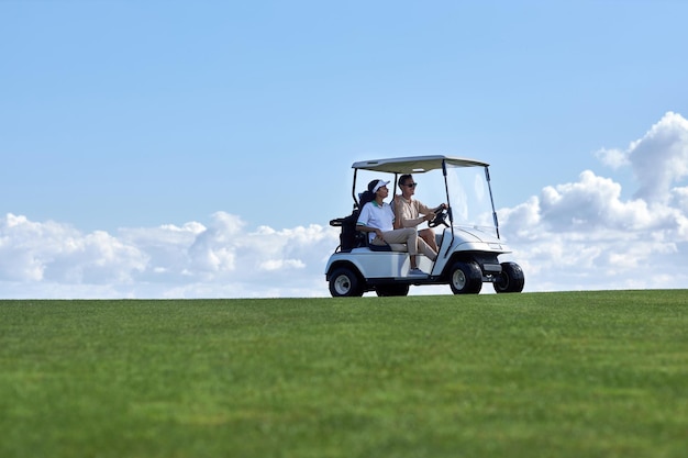 Couple driving golf cart across field