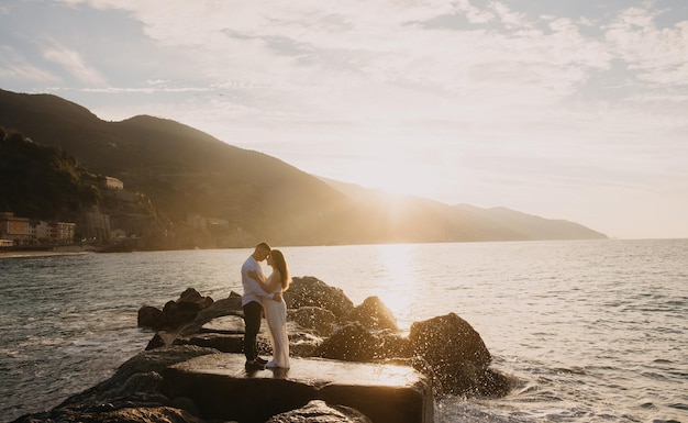 A couple embraces on a rock in front of a sunset.