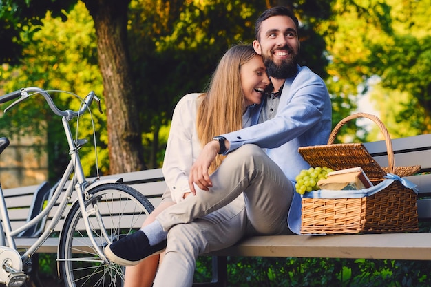 A couple enjoy a picnic on a bench in a park.