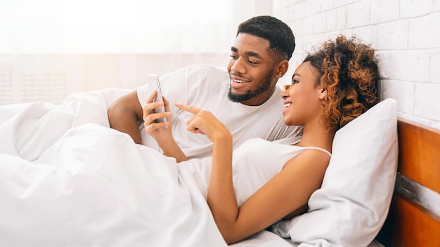 Couple enjoying mobile content in bed at home