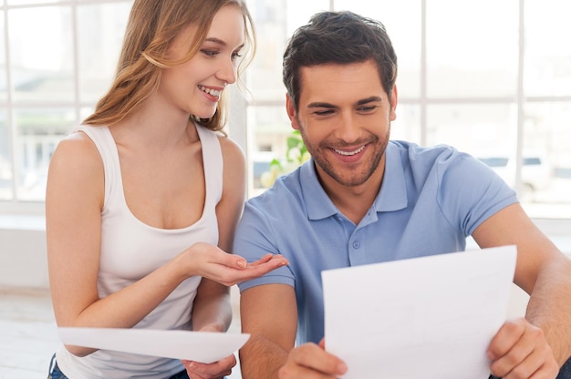 Couple examining documents. Cheerful young couple examining documents while sitting close to each other at their apartment