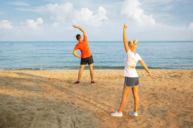 Couple family strong sporty sportswoman sportsman woman man in sport clothes warm up training do stretch exercise on sand sea ocean beach outdoor