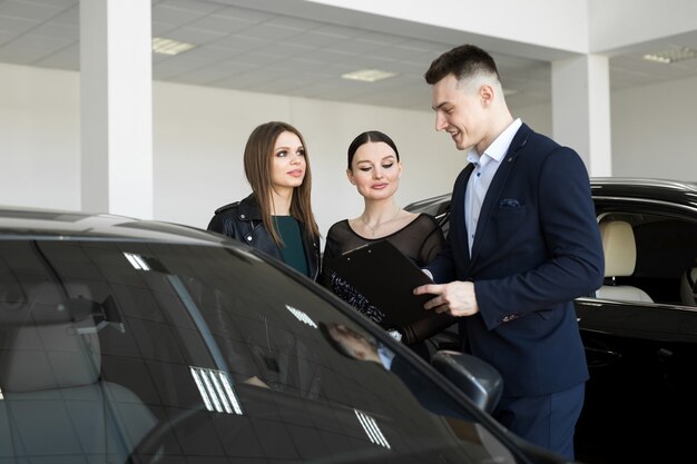 Couple of friends of girls with a car dealer choose a car in a car dealership