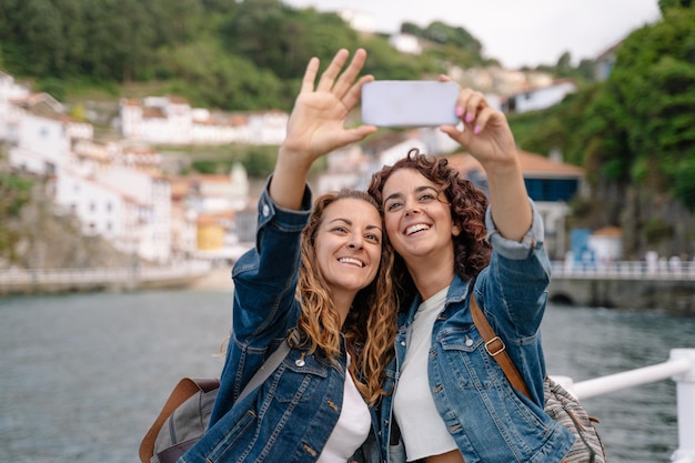 Couple of friends taking a picture with smartphone. Horizontal view of women traveling backpacking. Travel and technology lifestyle.