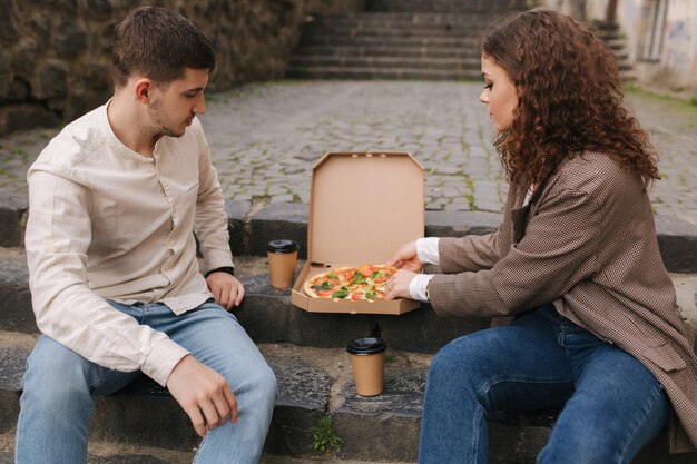 Couple grab slices of pizza from box at the outdoor