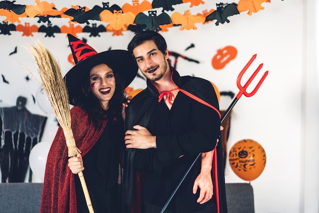 Photo couple having fun holding pumpkins and wearing dressed carnival halloween costumes and makeup posing with bats and balloons