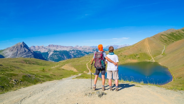 Couple of hikers on the mountain top looking at blue lake and mountain peaks