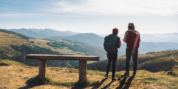 Couple of hikers with backpacks in front of landscape valley view on top of a mountain