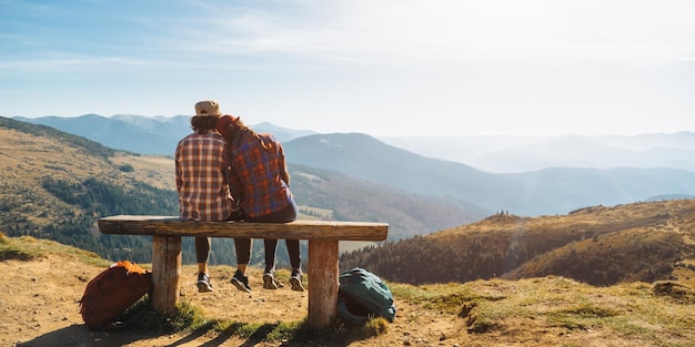 Couple of hikers with backpacks in front of landscape valley view on top of a mountain