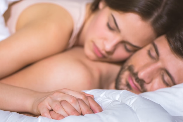 The couple hold hands and lay in the bed