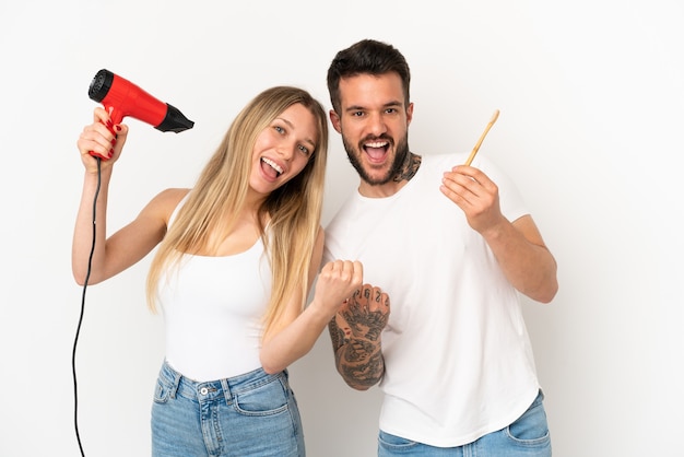 Couple holding a hairdryer and brushing teeth over isolated white background celebrating a victory