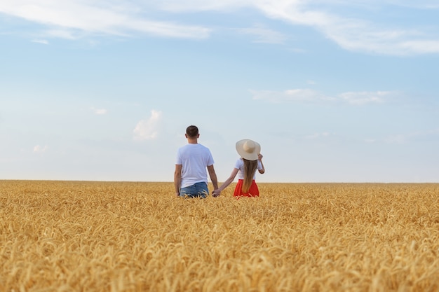 Couple holding hands and standing in wheat field. Rear view.