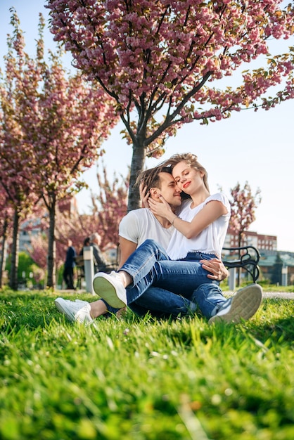 Couple hugs near sakura trees in blooming garden.