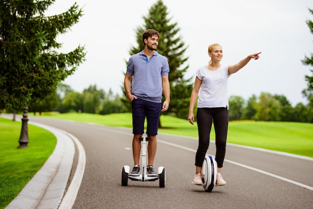 Couple is riding a gyroboard and a monocle in the park.