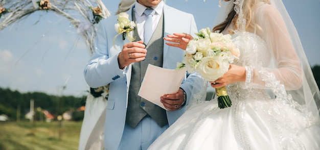 Couple is walking at the wedding ceremony outdoors Bride and groom holding arms Arch with flowers