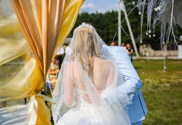 Couple is walking at the wedding ceremony outdoors Bride and groom kissing Arch with flowers