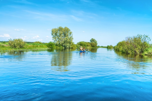 Couple at kayak trip on blue river landscape and green forest with trees blue water clouds sky