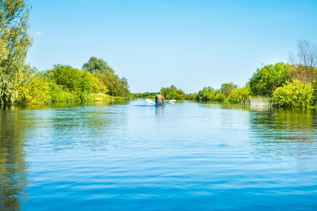 Couple at kayak trip on blue river landscape and green forest with trees blue water clouds sky