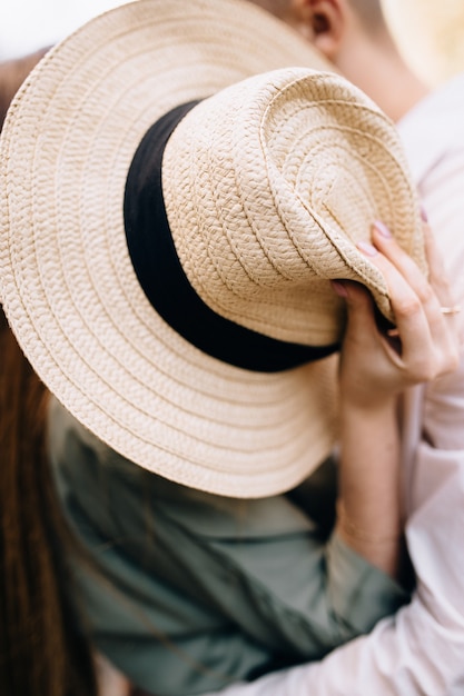 Couple kissing covering their faces with a straw hat.