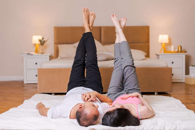 Couple lies on floor against background bed raised their legs and up girl