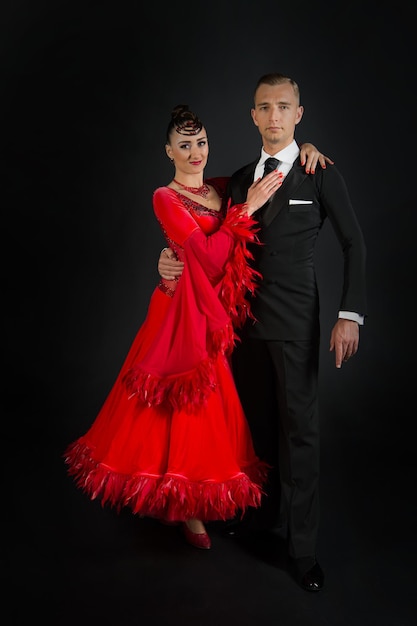 Couple in love, ballroon dance couple in red dress and black tuxedo on black background