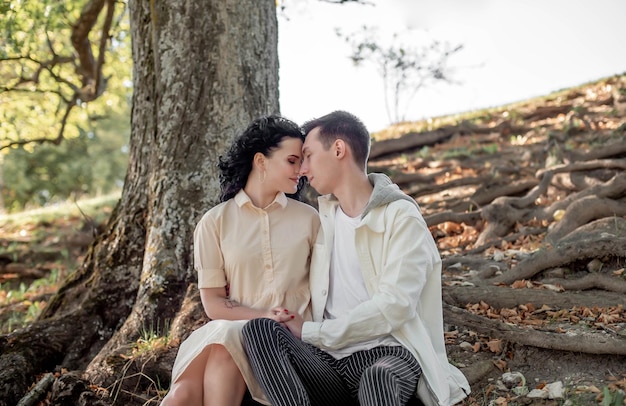 A couple in love, a couple and a girl sit under a beautiful tree and caress each other, kiss