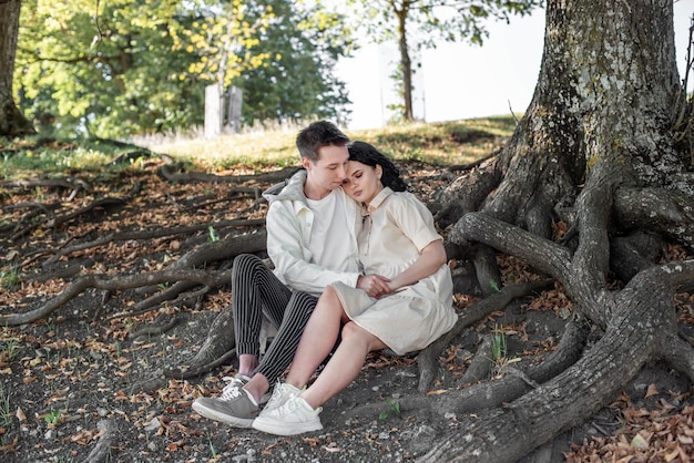 A couple in love, a couple and a girl sit under a beautiful tree and caress each other, kiss