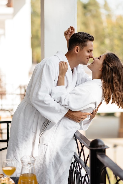 A couple in love cuddling on a hotel balcony in their bathrobes with breakfast on the table