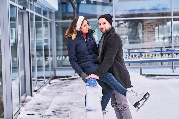 Couple in love, date at the ice rink, a girl sitting on a guardrail and embracing with her boyfriend.