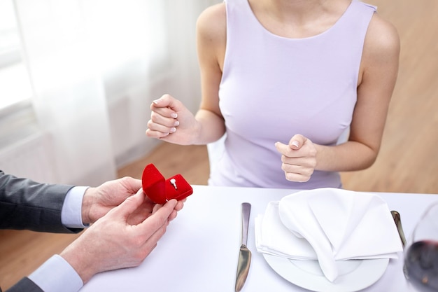 couple, love, engagement and holiday concept - close up of excited young woman and boyfriend giving her ring at restaurant