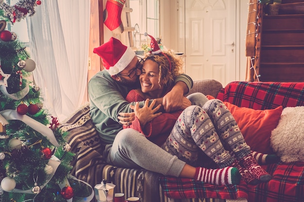 Couple in love enjoy and celebrate christmas eve morning at home hugging and kissing sit down on a coloured and decorated sofa at home