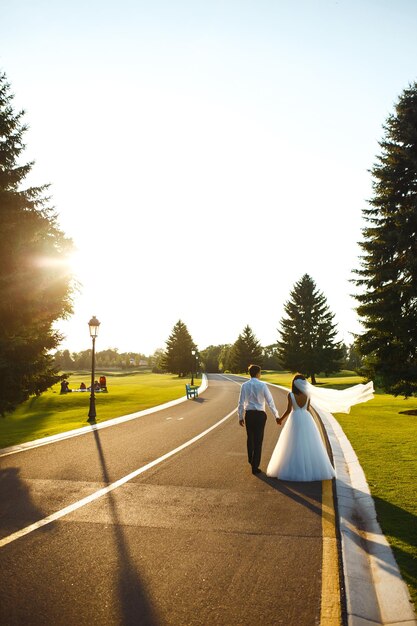 Couple in love go hand in hand on road to meet the sunset Bride and groom are walking on the road