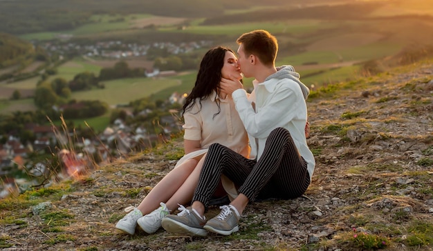 couple in love, a guy and a girl are sitting on a mountain at sunset kissing and hugging